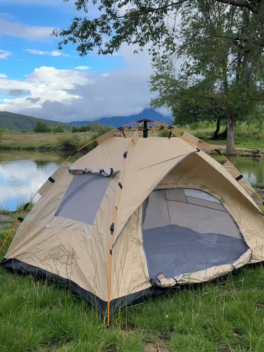 Instant pop-up camping tent set up in a grassy area near water with mountains in the background