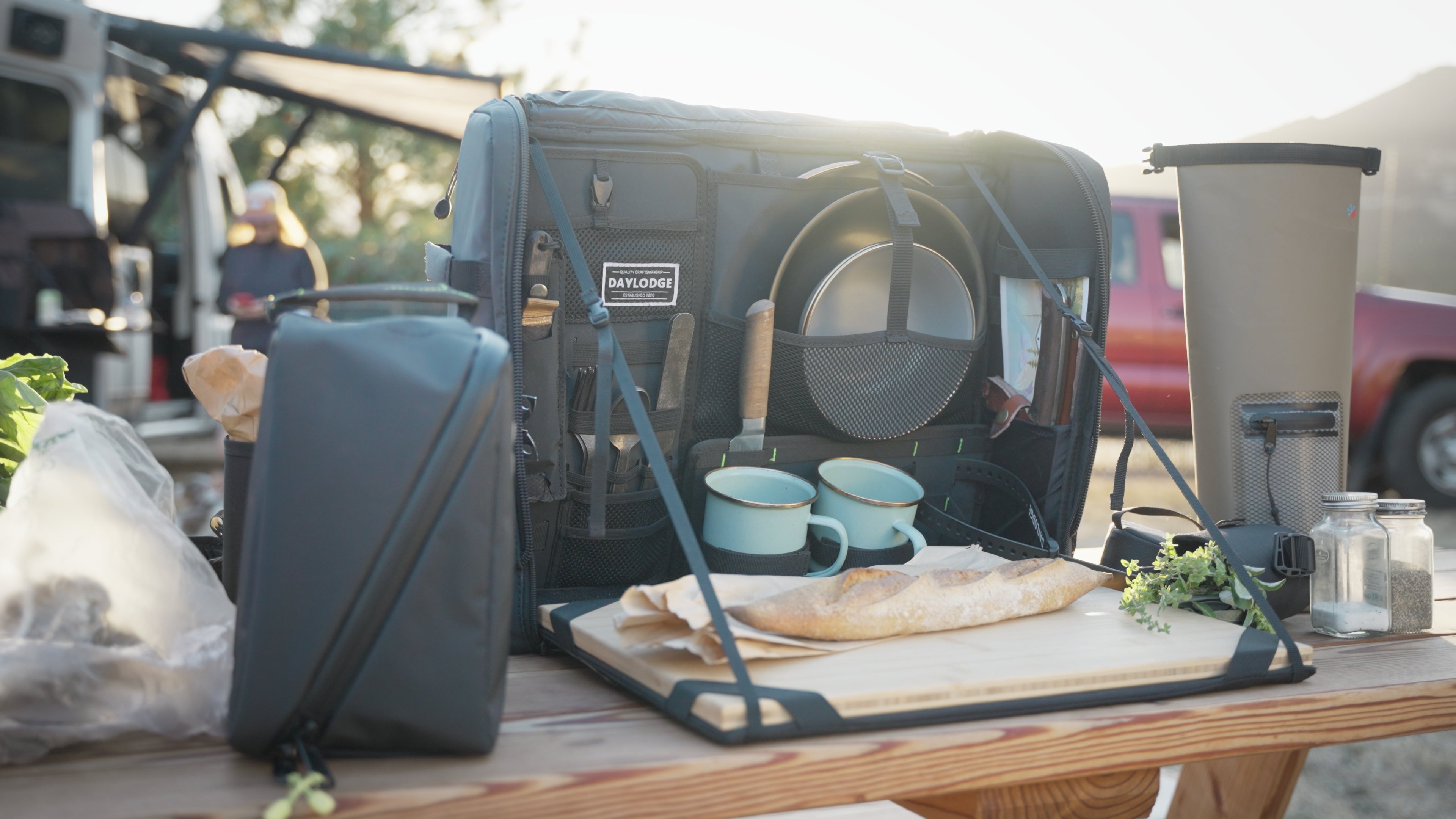 Outdoor setting with a portable kitchen setup on a table, including a cooler and cooking utensils.