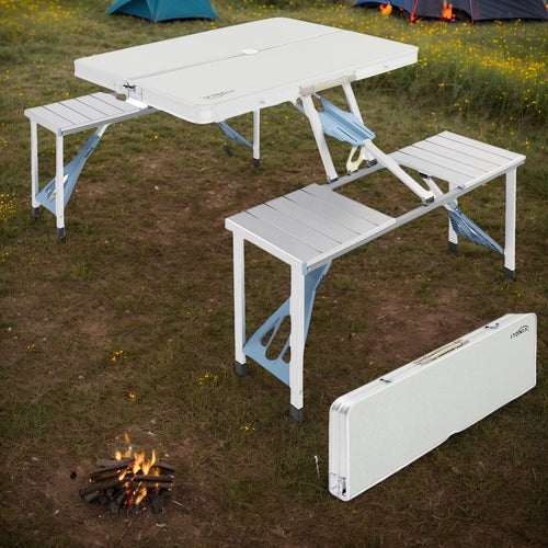 Portable camping table with benches set up outdoors near a campfire.