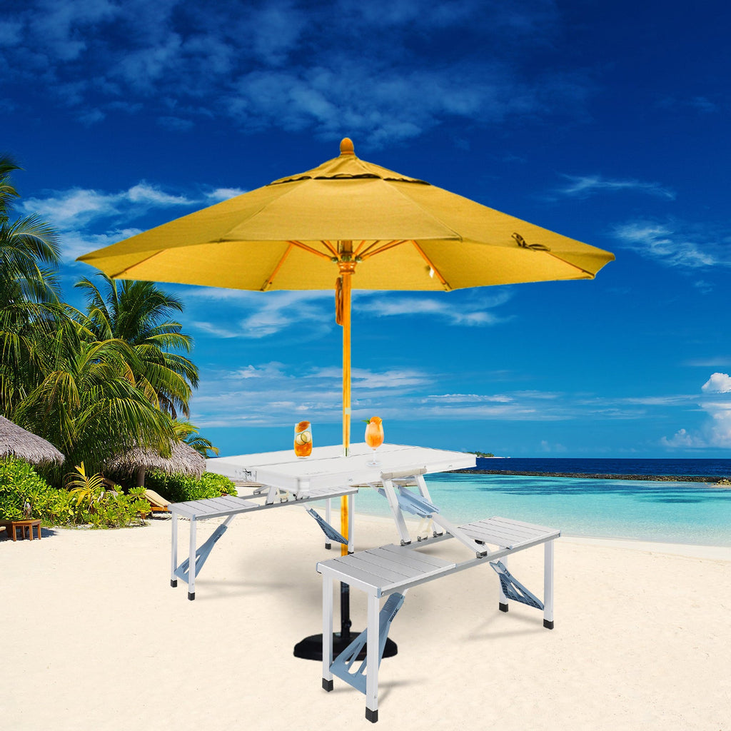 Yellow umbrella on a white table with chairs on a sandy beach with ocean and sky in the background