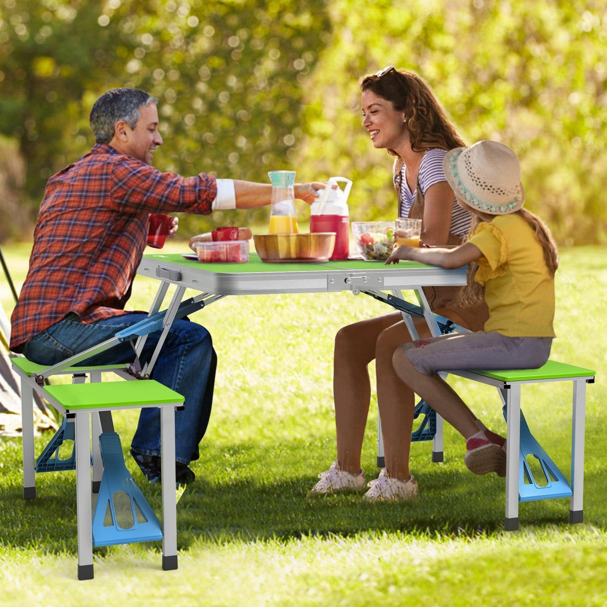 Family of three enjoying a picnic at a park with a portable folding table.