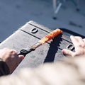 Person securing a black suitcase with an orange strap outdoors.